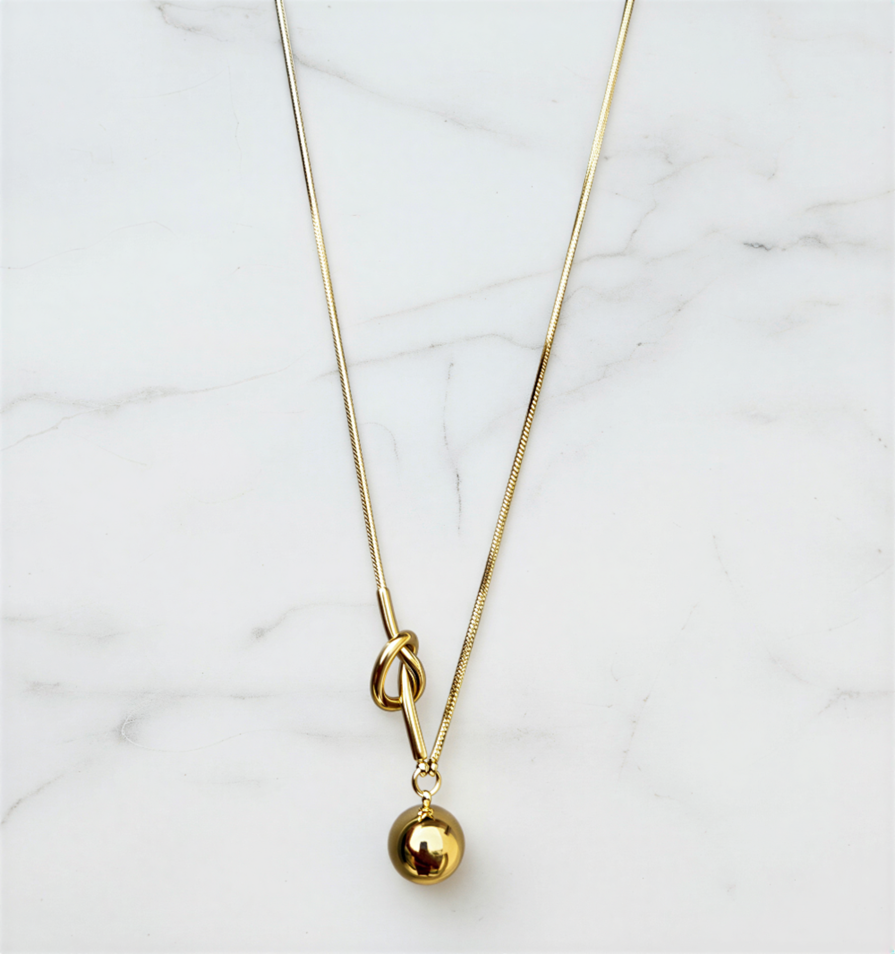 Gold necklace with a small gold ball pendant on a marble surface