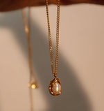 Gold necklace with a pearl pendant on a neutral background