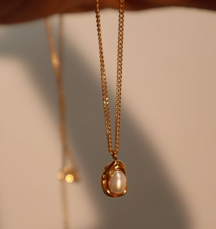 Gold necklace with a pearl pendant on a neutral background