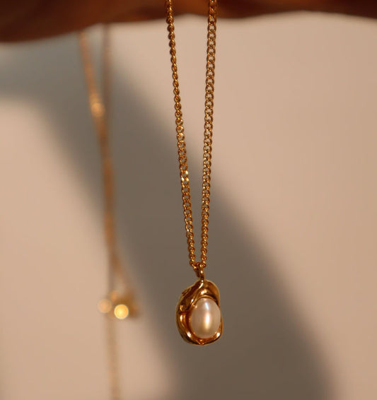 Gold necklace with a pearl pendant on a neutral background