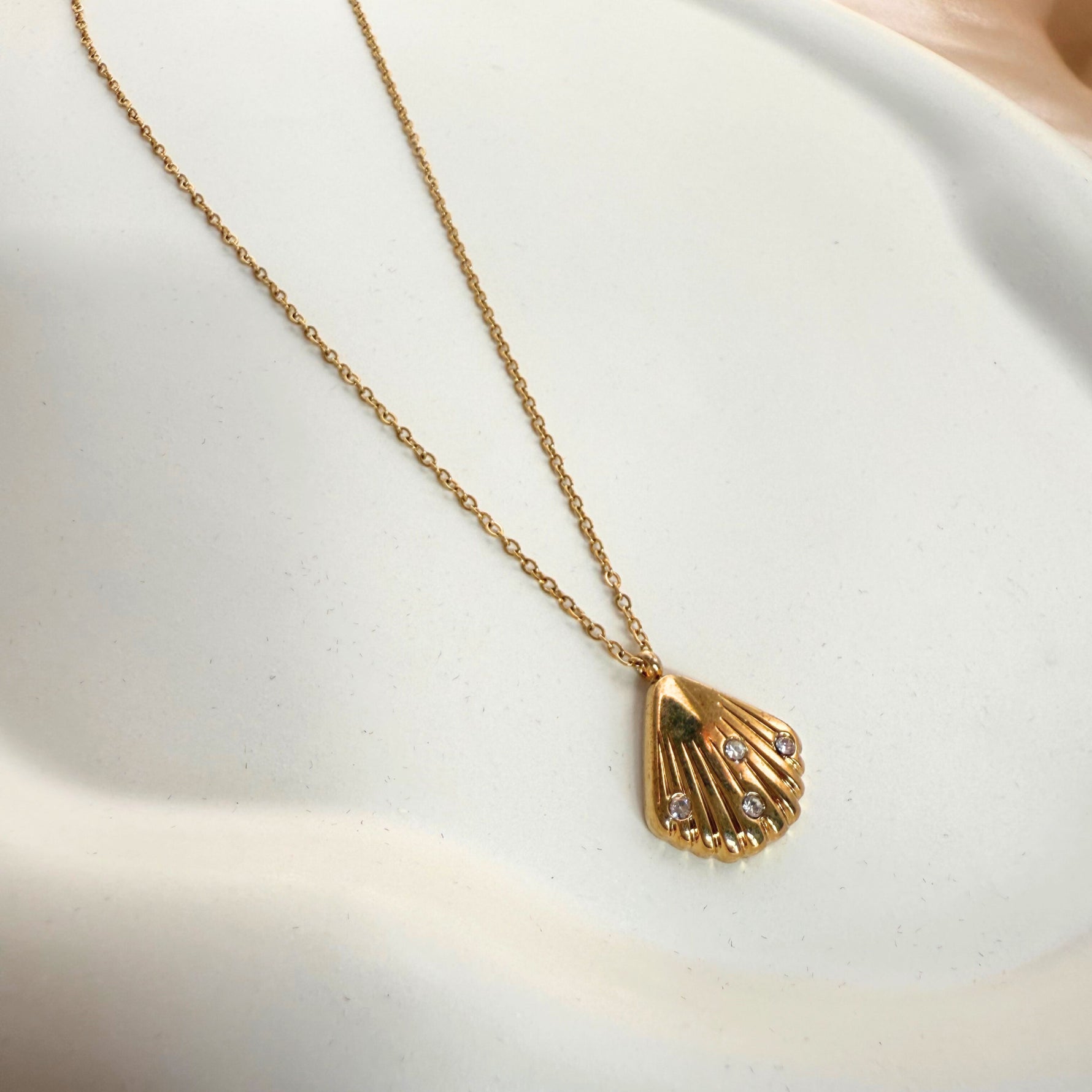 A gold-colored necklace with a shell-shaped pendant, displayed on a white surface.
