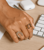 Hand wearing gold rings on a desk with a keyboard in the background