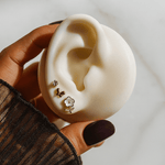 Hand holding a white ear model with earrings displayed on a neutral background