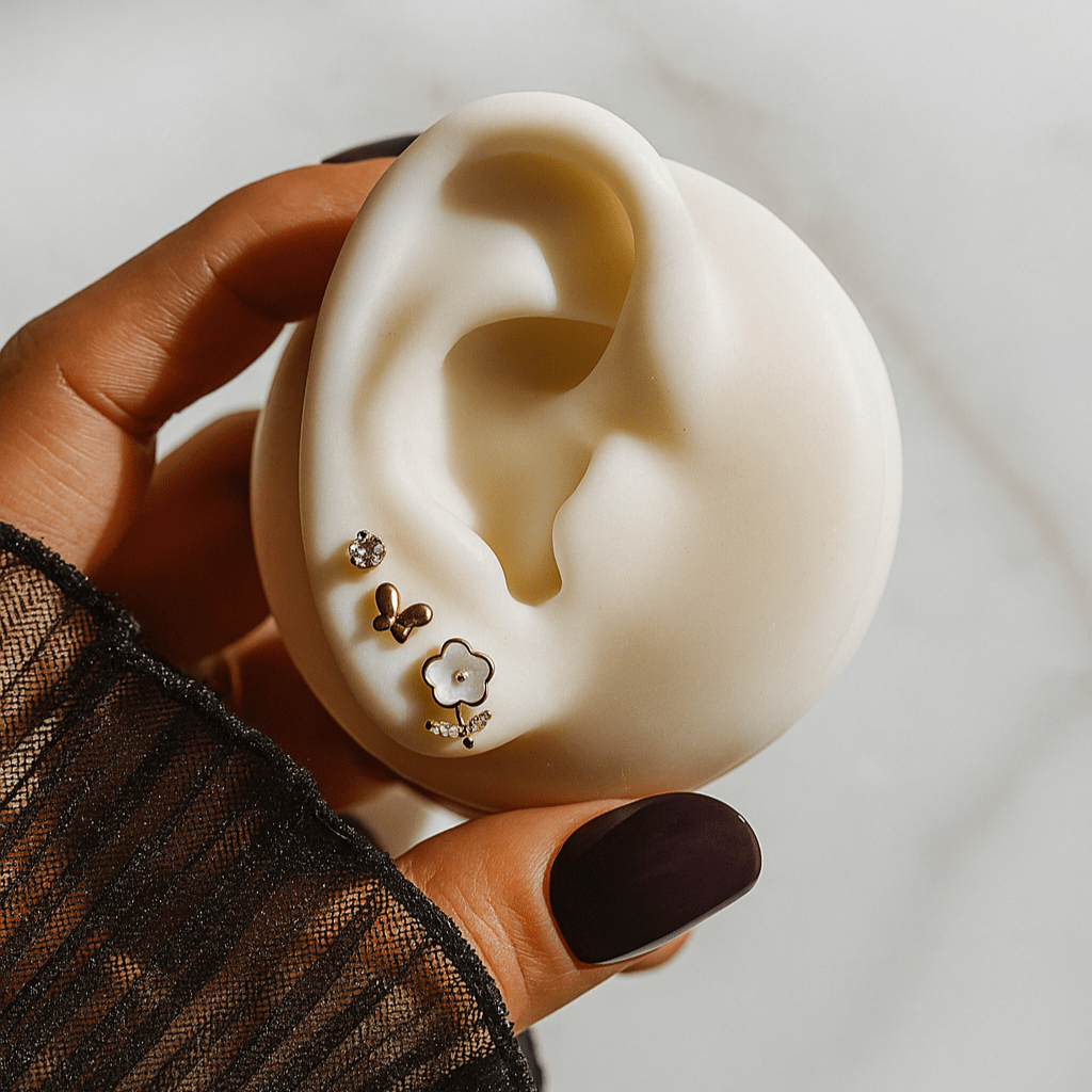Hand holding a white ear model with earrings displayed on a neutral background