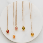 Four gold necklaces with colored gemstones on a white plate