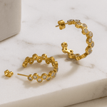 Gold hoop earrings with small diamonds on a marble surface