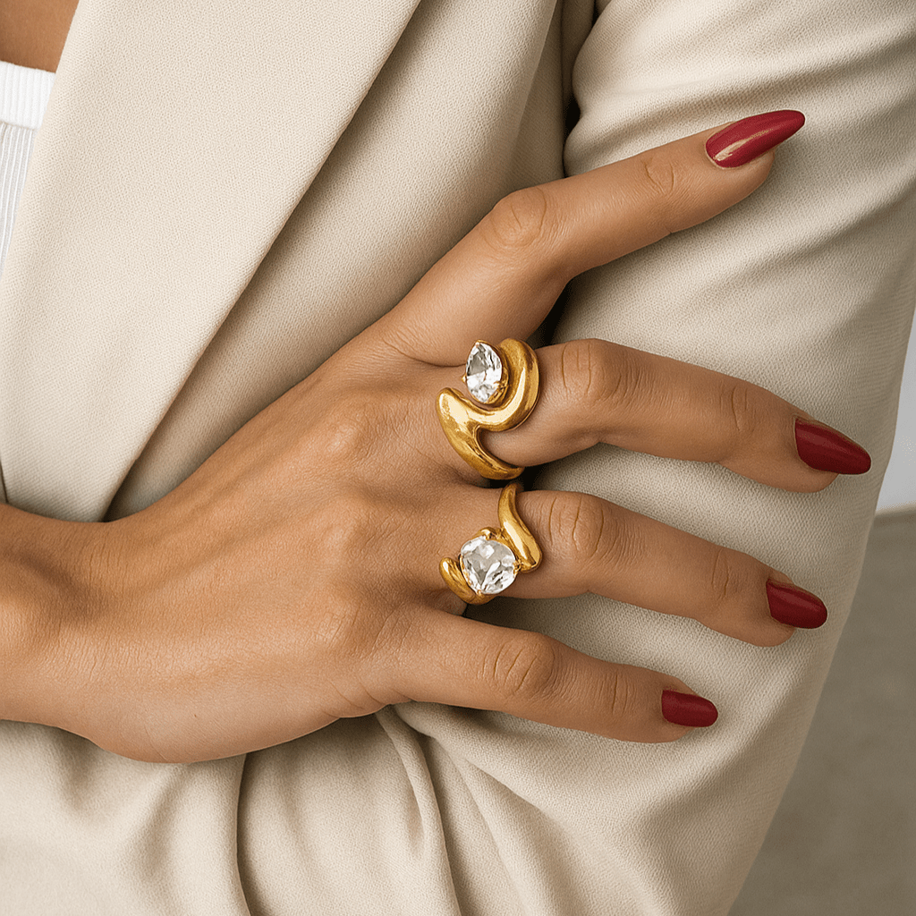 Hand wearing two gold rings with gemstones against a neutral background