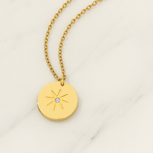 Gold necklace with a round pendant featuring a star design on a light background
