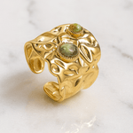 Gold ring with green gemstones on a marble surface