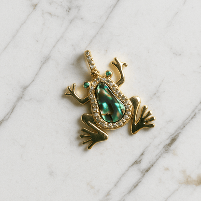 Gold frog pendant with green gemstone on a marble background