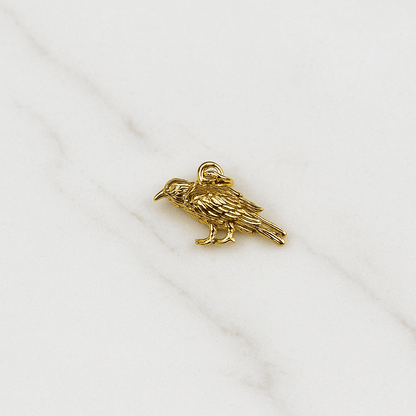 Gold bird charm on a white fabric background