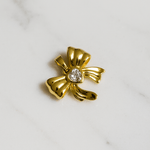 Gold bow-shaped brooch with a central gemstone on a marble background