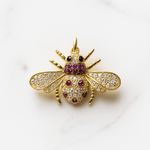 Gold bee-shaped pendant with gemstones on a white background