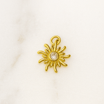Gold sun-shaped pendant with a central gemstone on a white background