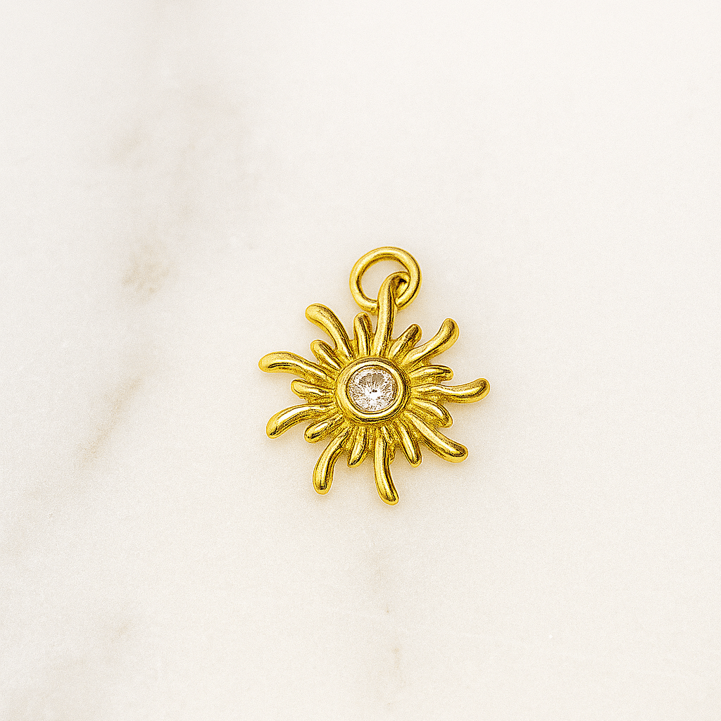 Gold sun-shaped pendant with a central gemstone on a white background