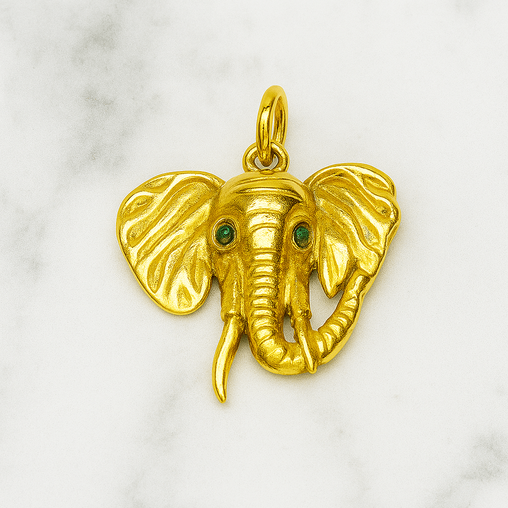 Gold elephant pendant with green eyes on a marble background