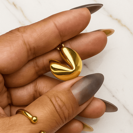 Gold leaf-shaped earring being held by a hand with a neutral background