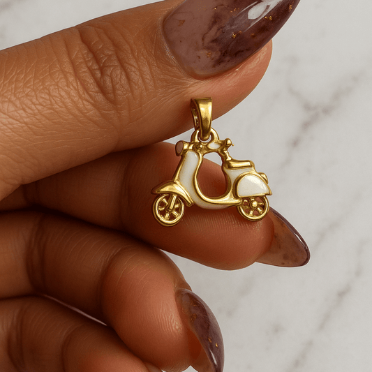 Gold carriage pendant held by a hand with maroon nail polish on a marble background
