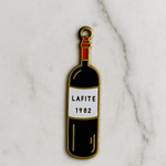 Enamel pin of a wine bottle labeled 'Lafite 1982' on a marble background