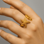 Hand wearing a gold starfish ring on a gray background