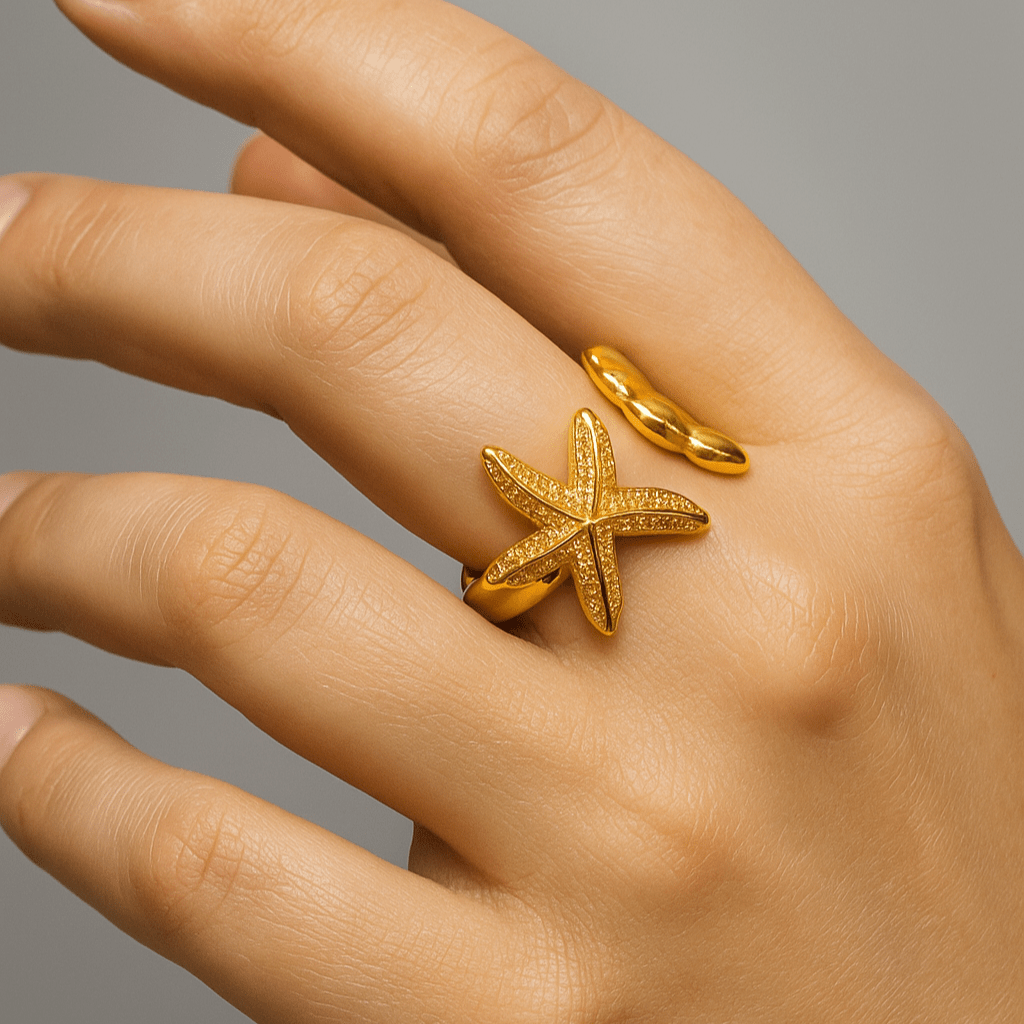 Hand wearing a gold starfish ring on a gray background