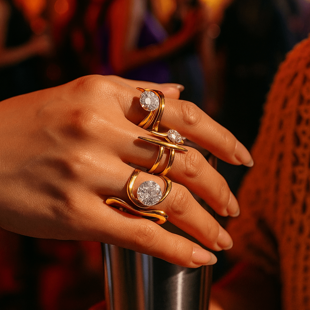 Hand wearing gold rings with gemstones against a blurred background of people and lights