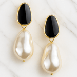Pair of earrings with black stones and pearl-like drops on a white marble background