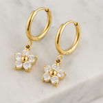 Gold hoop earrings with floral charms on a light background