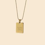 A gold-colored necklace with a square pendant that has 'MORE SELF LOVE' written on it, displayed against a light background.