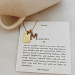 Gold necklace with 'M' pendant on a card with text and a mug in the background