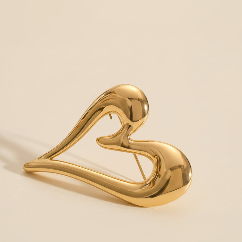 Gold heart-shaped brooch on a marble surface with a ceramic plate in the background