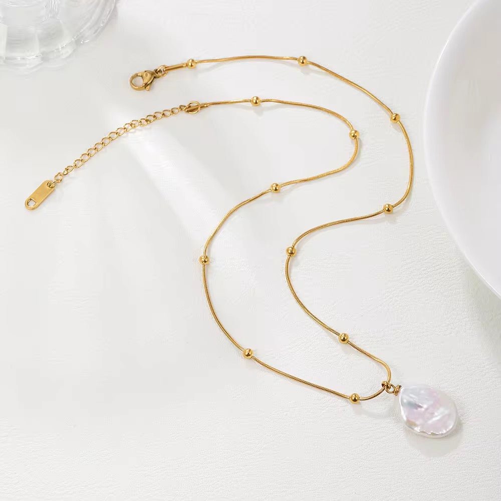 A gold-colored necklace with a single pearl pendant, displayed on a white surface.