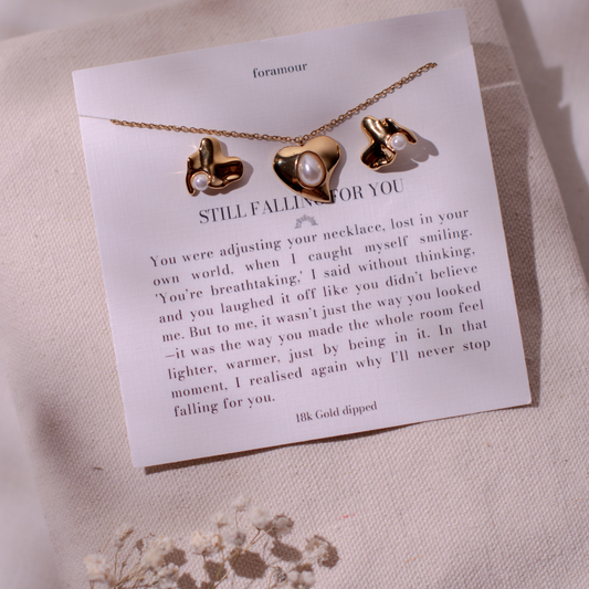 A gold-plated necklace with a heart-shaped pendant and a pair of earrings, presented on a card with a love-themed message.