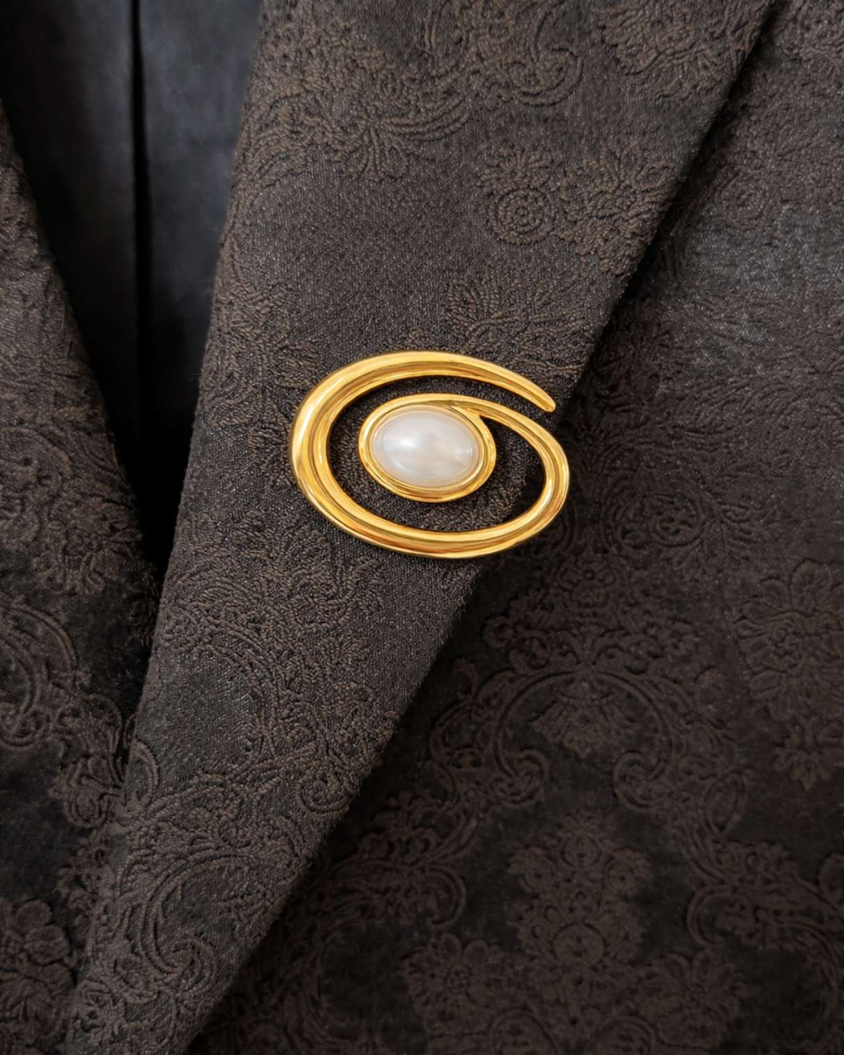 Gold brooch with a pearl on a dark textured fabric background