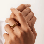 A person's hand wearing an 18kt gold plated, adjustable ring with a spherical accent and rectangular detail.
