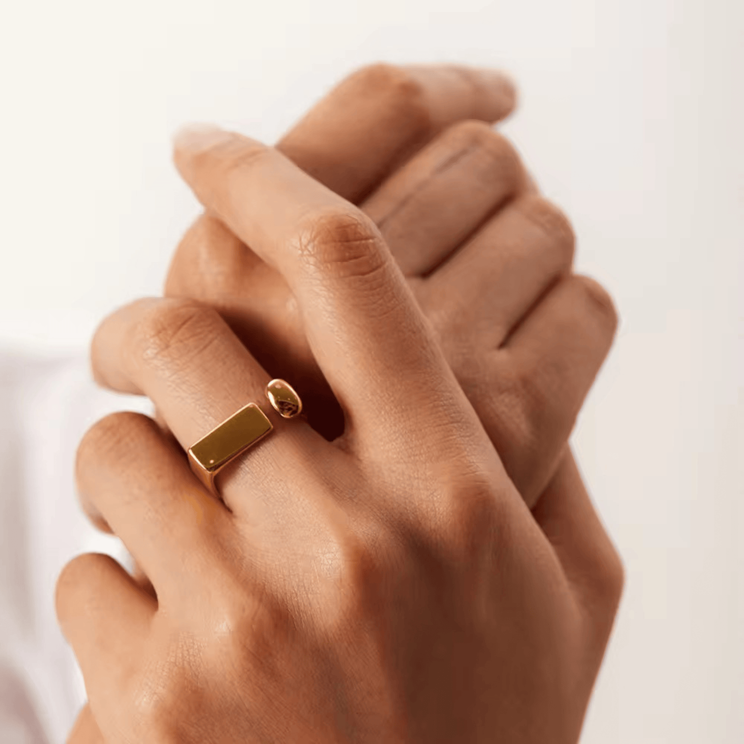 A person's hand wearing an 18kt gold plated, adjustable ring with a spherical accent and rectangular detail.