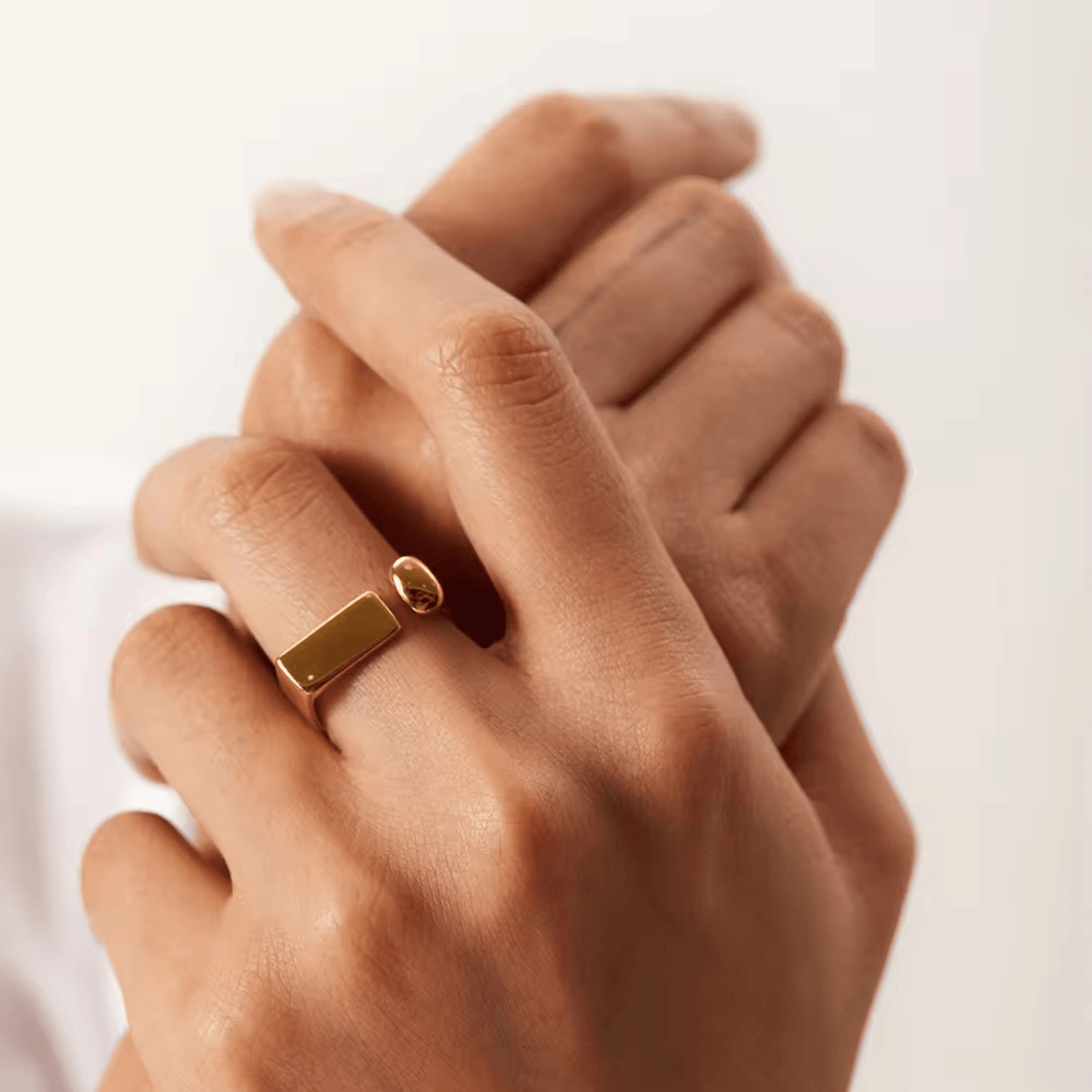 A person's hand wearing an 18kt gold plated, adjustable ring with a spherical accent and rectangular detail.