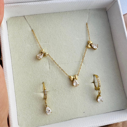 A gold pendant necklace with delicate bows and radiant teardrop stones, worn by a person.