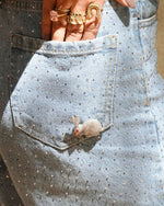 Close-up of a decorative mouse pin on a denim pocket with jewelry in the background.