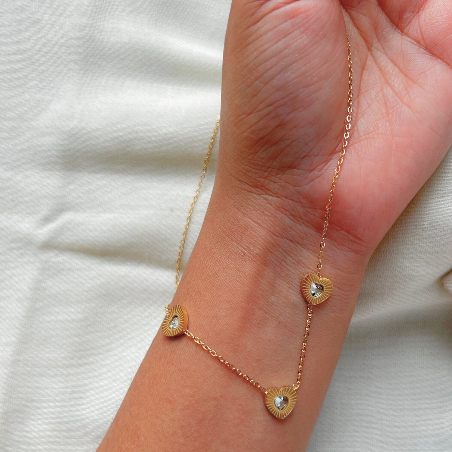 A gold-tone necklace with heart-shaped pendants on a hand, displaying the delicate and radiant design.