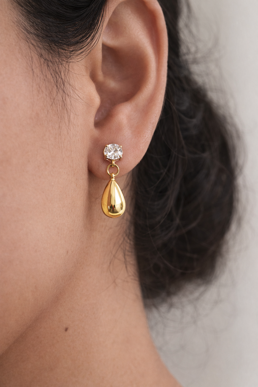 Gold earring with a clear gemstone worn by a person