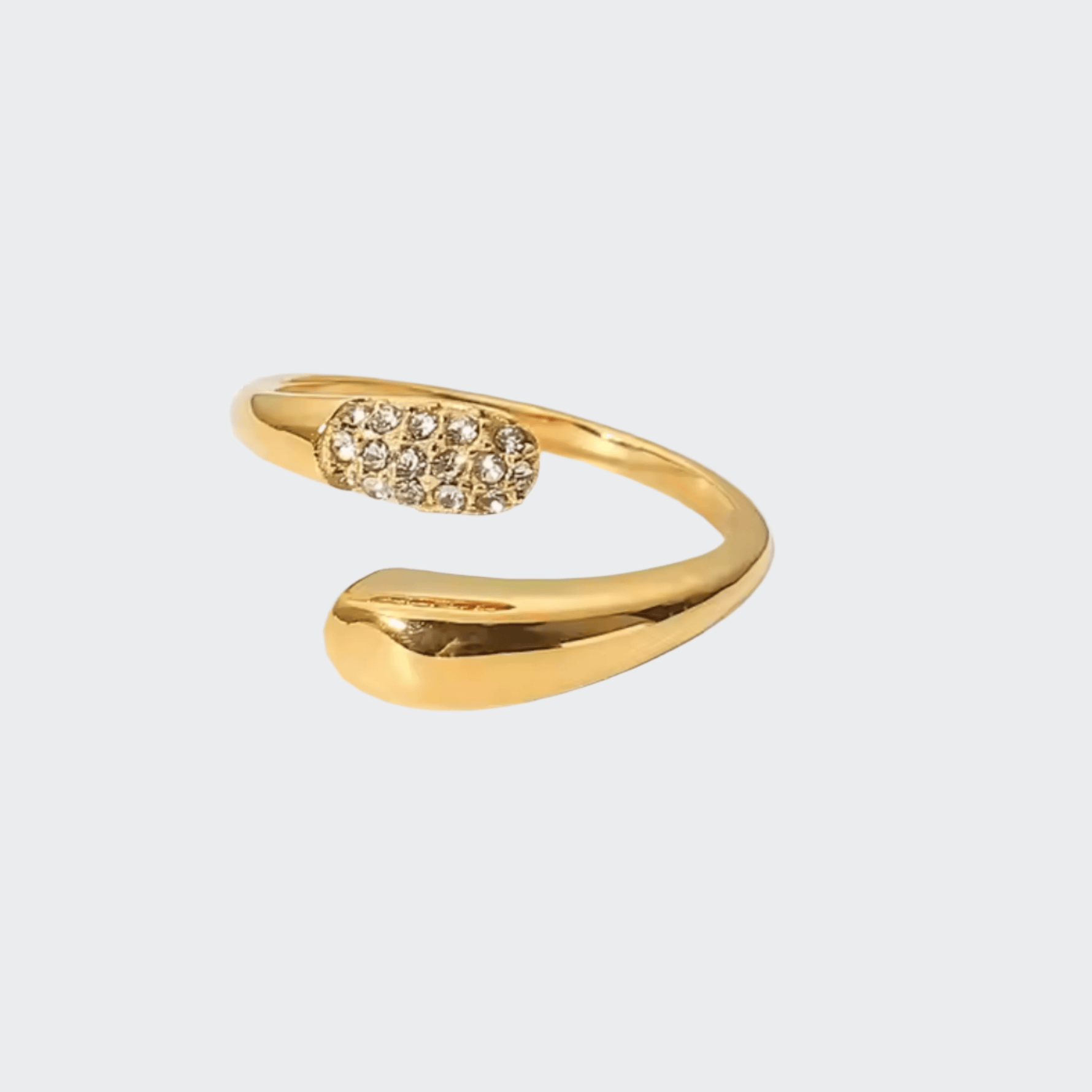 A gold-colored, adjustable ring with a band that has a smooth finish and a small, circular, studded detail on one side.
