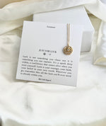 Necklace with a gold pendant on a card with text on a white fabric background