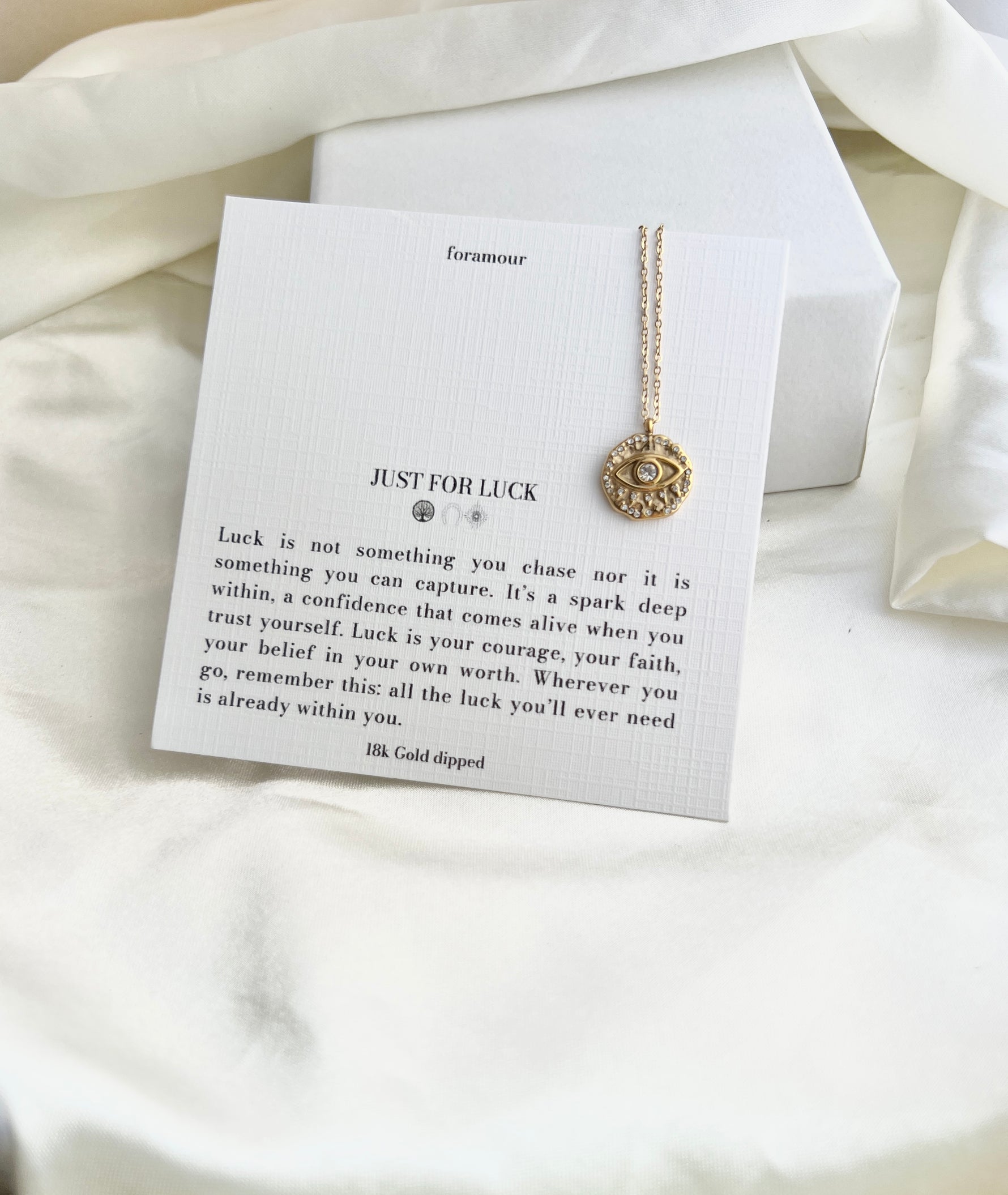 Necklace with a gold pendant on a card with text on a white fabric background