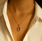 Gold necklace with a red pendant worn by a person in a white shirt.