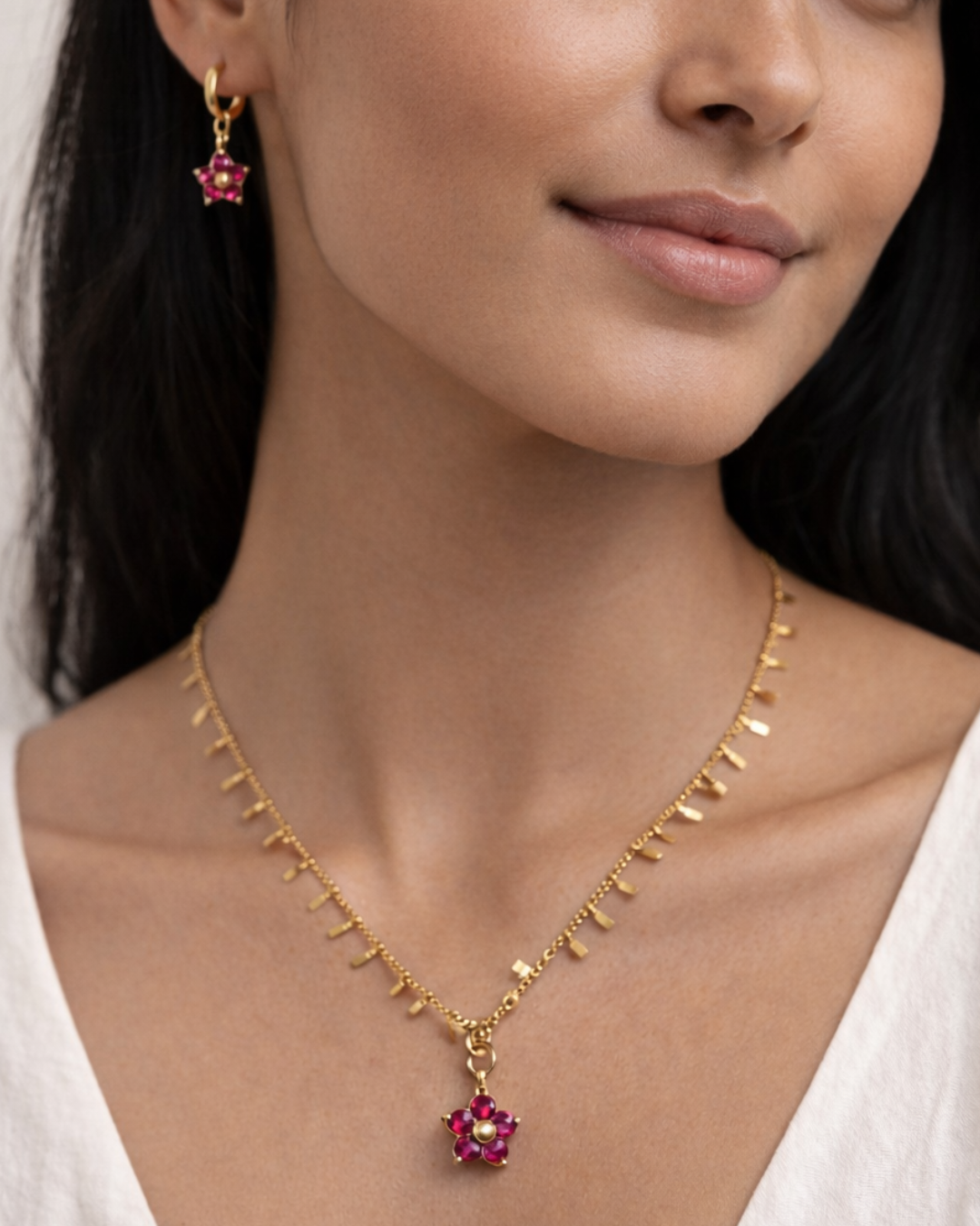 Woman wearing a gold necklace with a pink flower pendant and matching earrings.