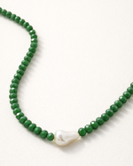 Green beaded necklace with a white pearl pendant on a white background