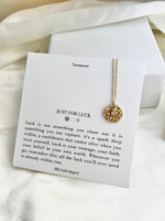 Necklace with evil eye pendant on a card with text, placed on a white fabric background