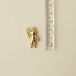 Gold charm resembling an astraunaut, next to a ruler for scale.
