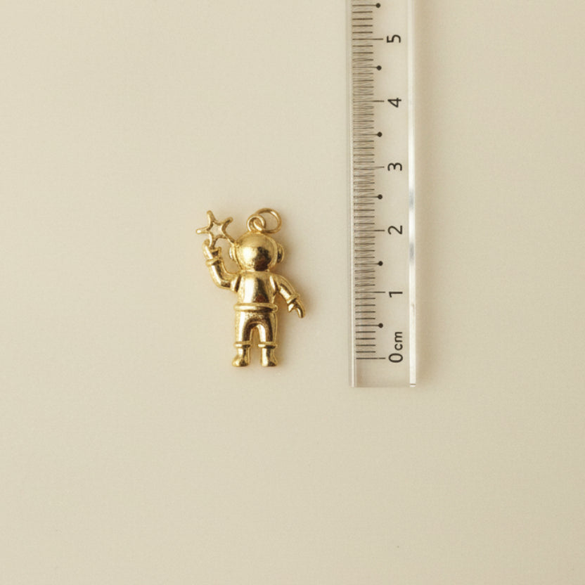 Gold charm resembling an astraunaut, next to a ruler for scale.